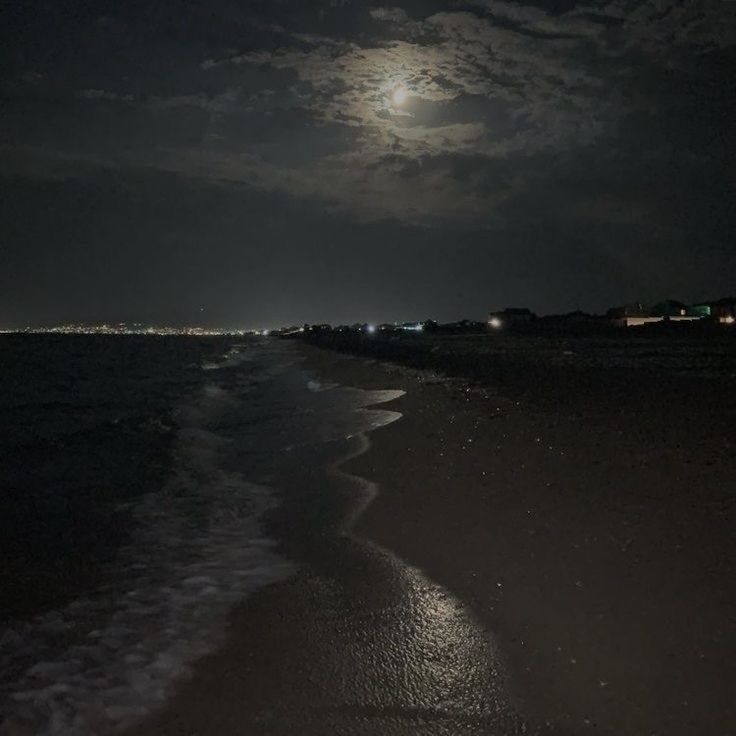 the moon is shining over the water at night on the beach with waves coming in