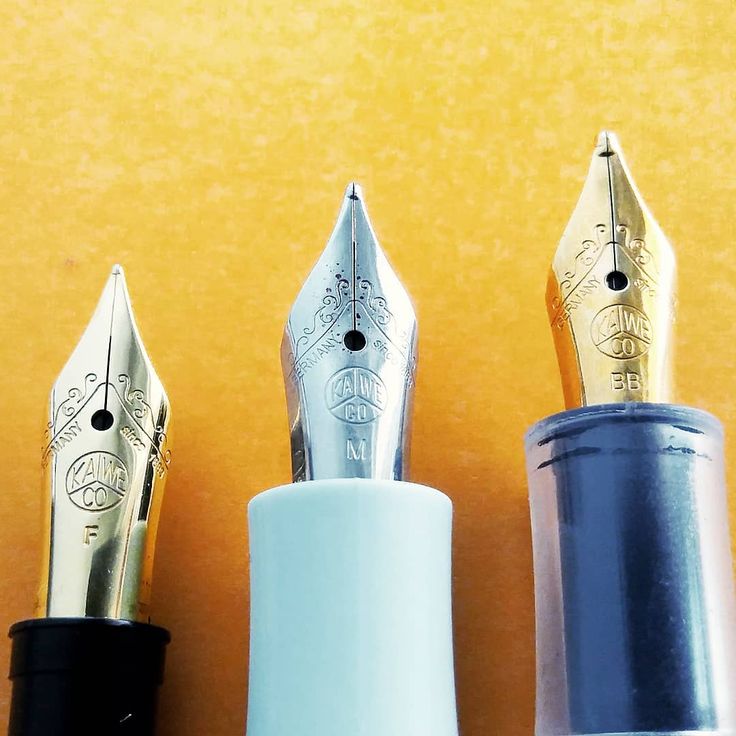 three fountain pens lined up next to each other on a yellow surface with one pen in the middle