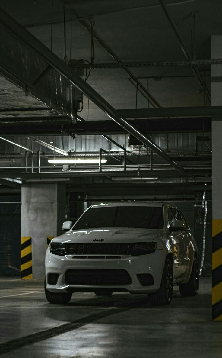 a white car parked in a parking garage next to yellow and black striped lines on the floor