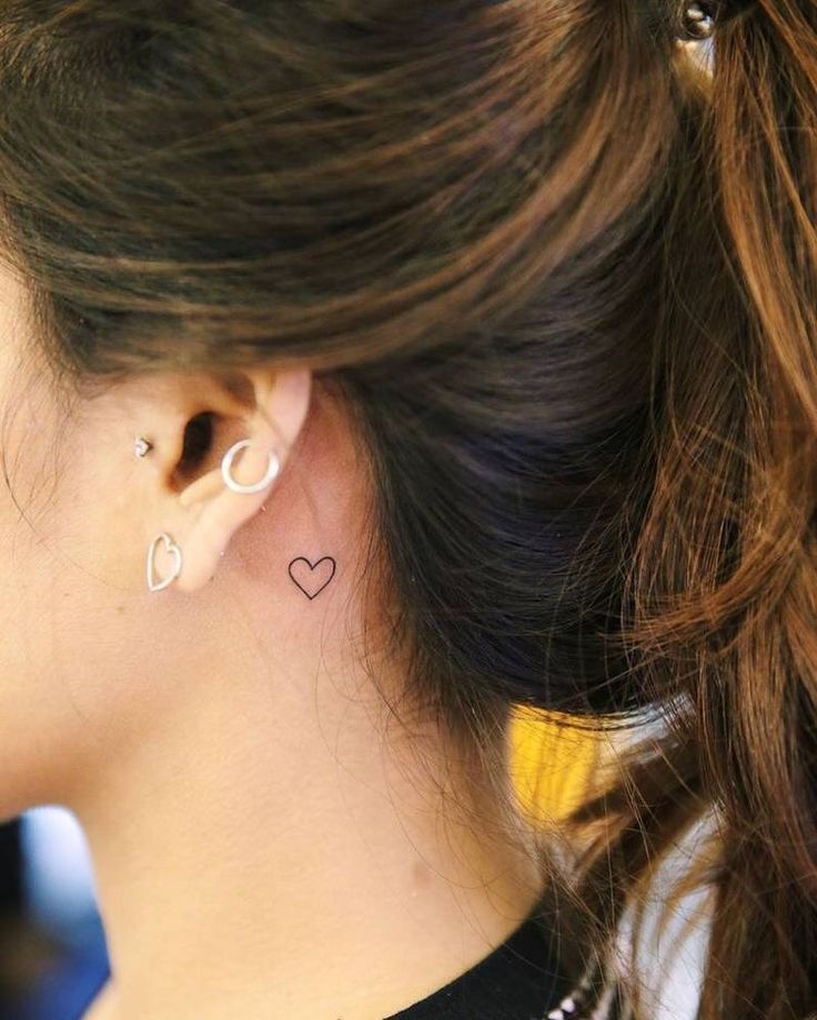 a woman wearing ear piercings with a heart tattoo on her left side of the ear