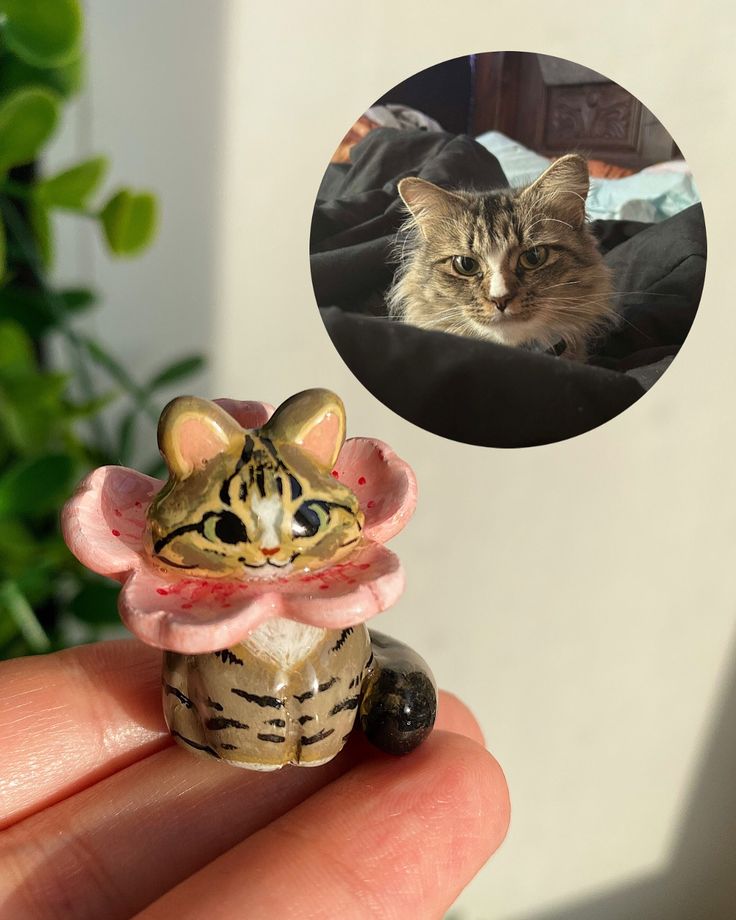 a small cat figurine is sitting on someone's hand with a photo in the background