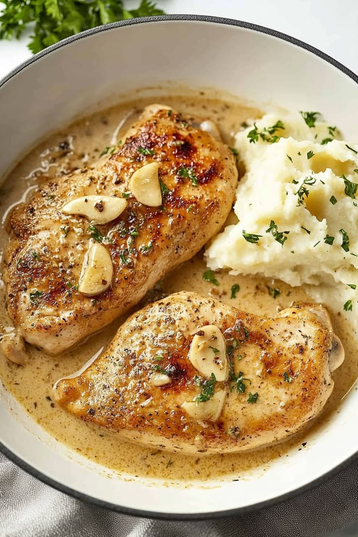 two pieces of chicken with potatoes and gravy in a white bowl