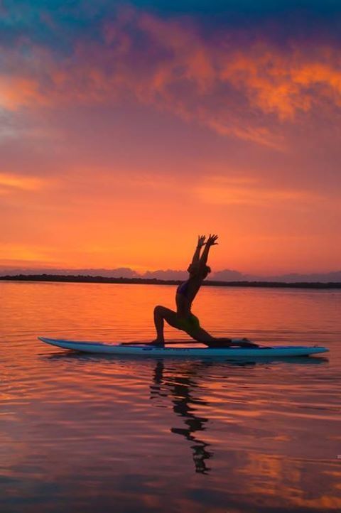 a woman on a surfboard in the water at sunset with her arms raised up