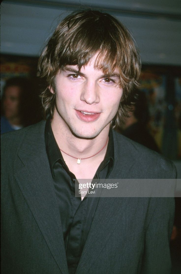 the young man is wearing a suit and black shirt with his hair pulled back into a ponytail