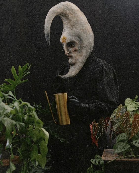 a creepy looking man holding a cup in front of some potted plants and greenery