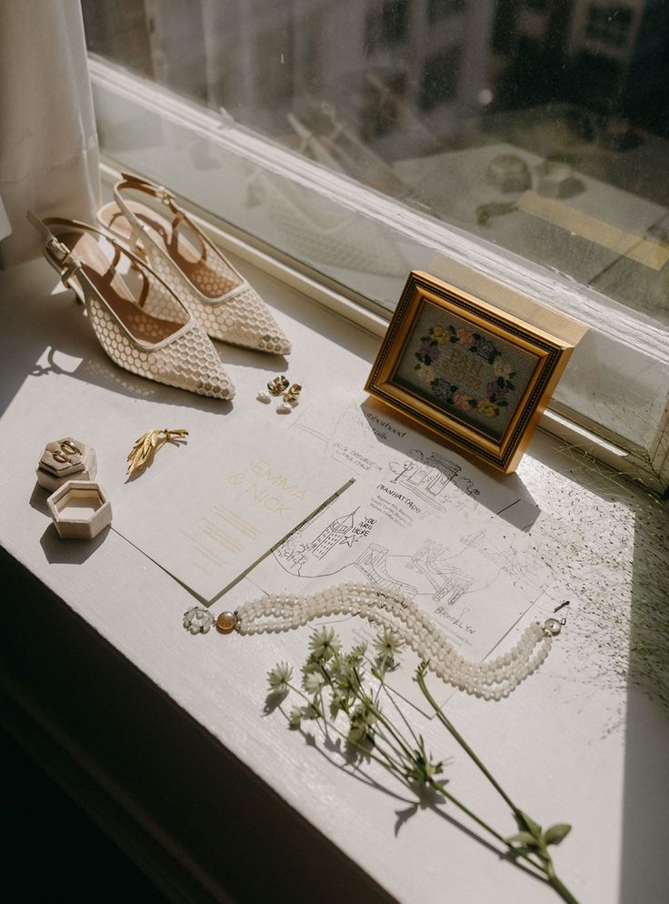 shoes and jewelry sit on a window sill in front of a framed photograph, which sits next to a flower