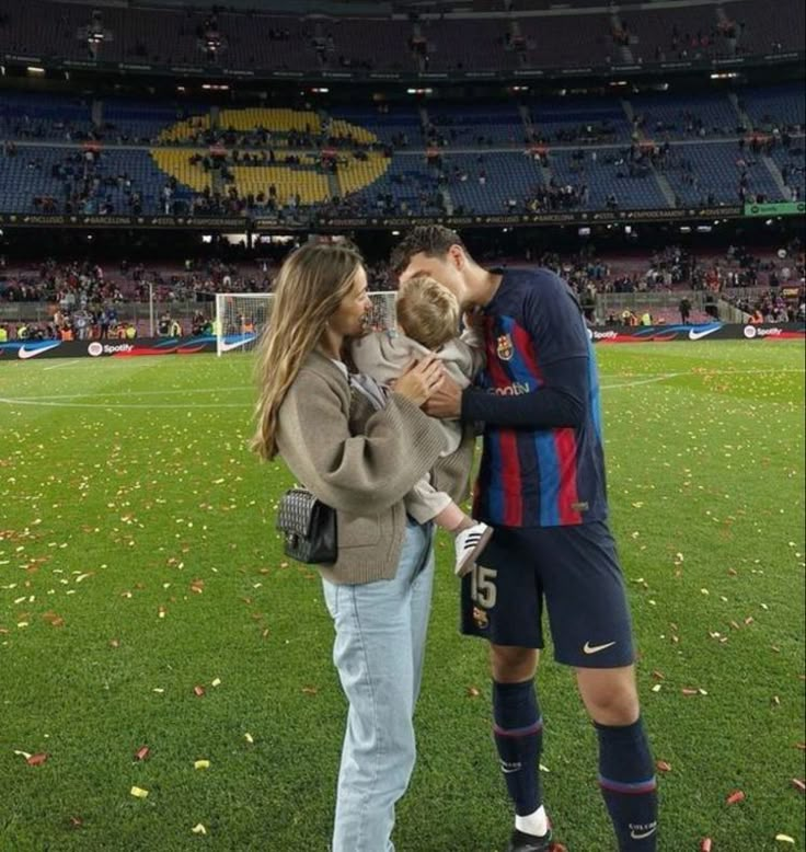 a man and woman holding a baby in front of a soccer field