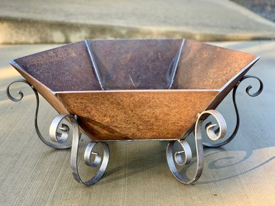 a metal wheelbarrow with wooden bowl on the top and wrought iron wheels around it