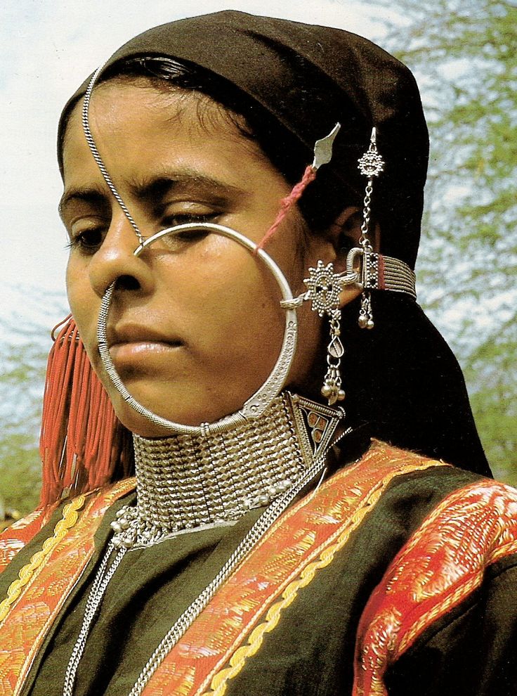 a woman in an elaborate head piece with chains and piercings on her nose is staring into the distance