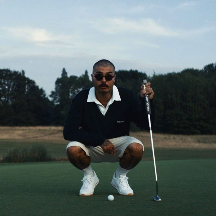 a man kneeling down to put a golf ball on the green in front of him