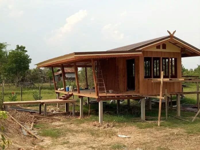 a small wooden house sitting in the middle of a lush green field on stilts