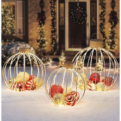 three decorative christmas balls sitting in front of a house with lights on the outside and inside