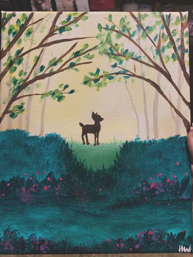 a person holding up a painting of a deer in the woods with trees and flowers