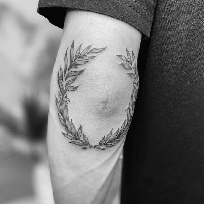 a black and white photo of a woman's arm with a wreath tattoo on it