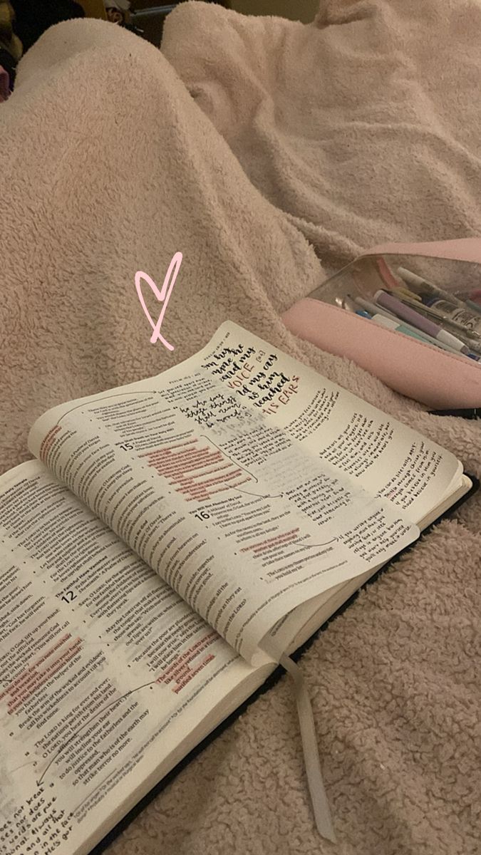 an open book laying on top of a bed next to a pink object in the shape of a v