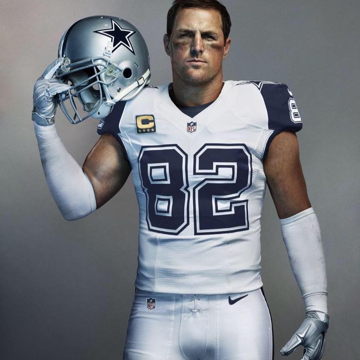 a football player holding a helmet and posing for a photo in front of a gray background