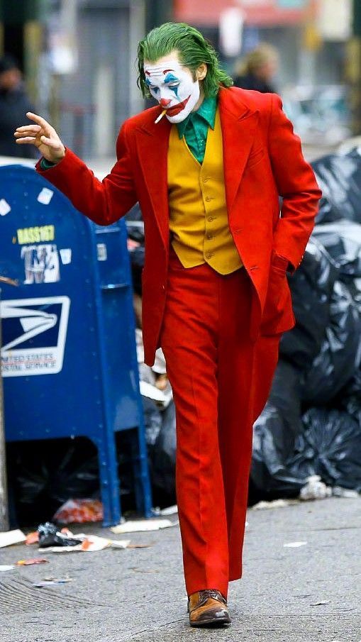 a man in a red suit and clown makeup walking down the street with his hands out