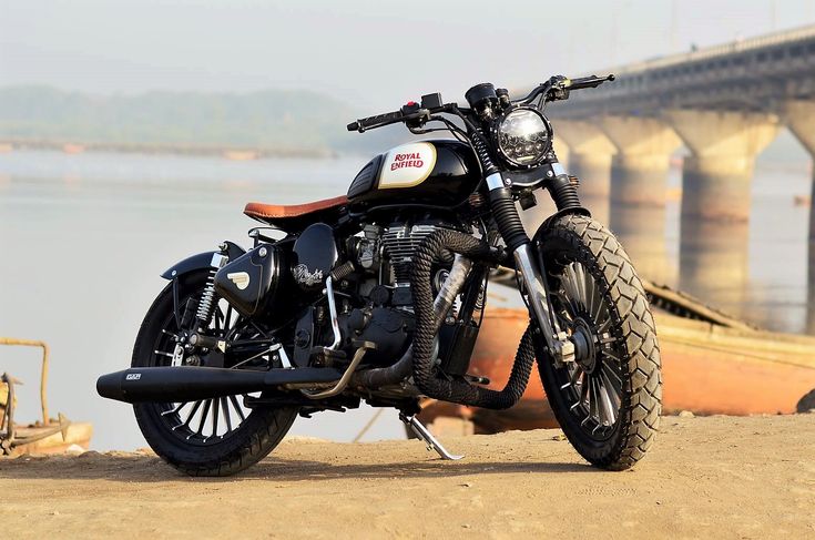 a motorcycle is parked on the beach next to some water and a bridge in the background