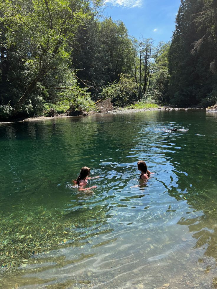 two people swimming in a river surrounded by trees