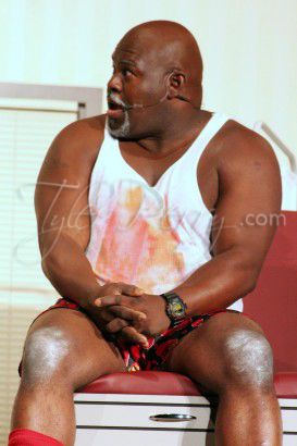 a man sitting on top of a red chair in front of a white wall with his legs crossed