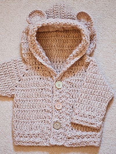 a crocheted sweater with a hood and buttons on the front is shown in beige