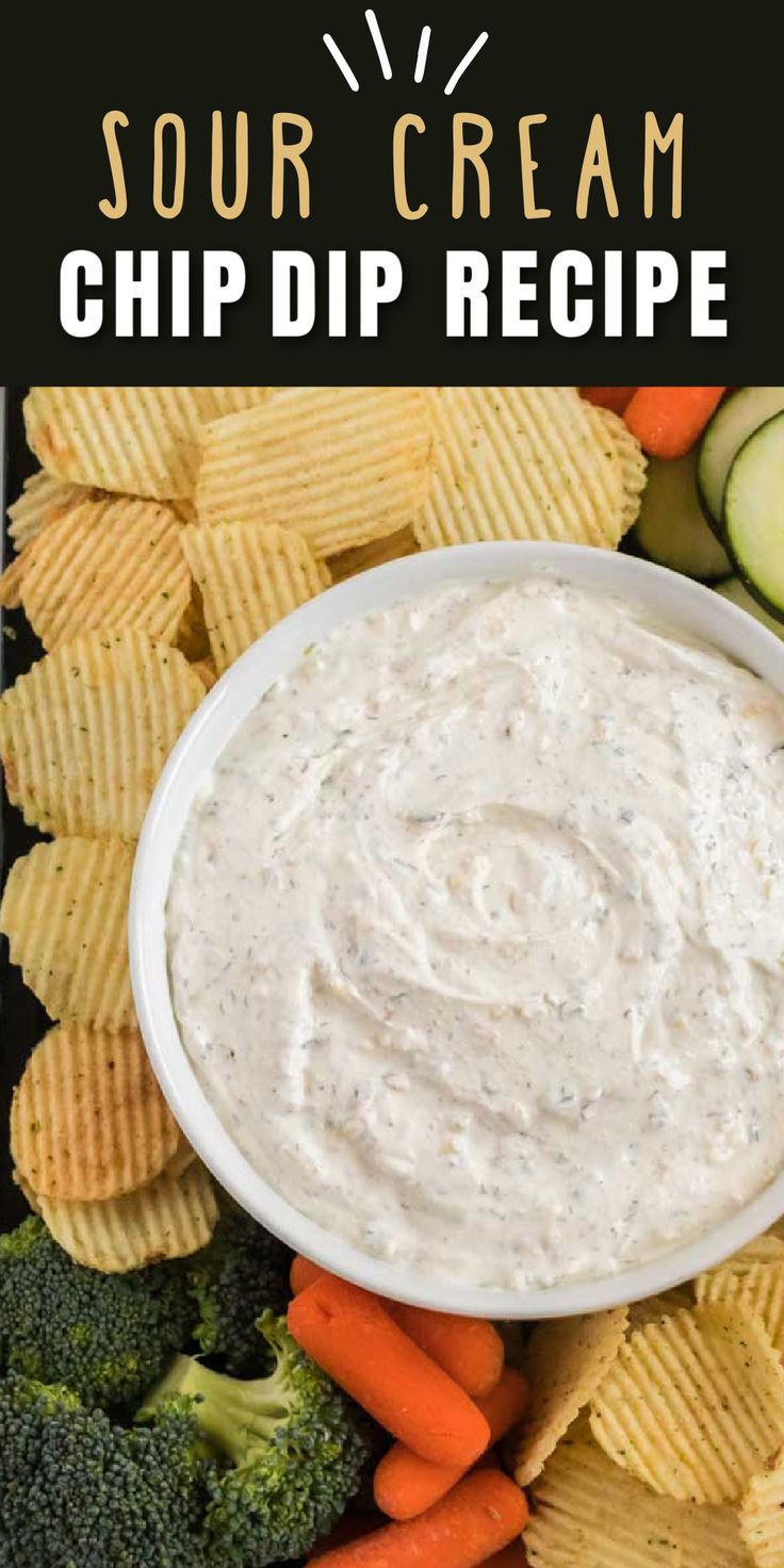 a white bowl filled with dip surrounded by veggies, chips and cucumbers