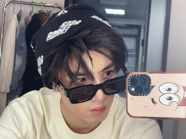 a young man wearing sunglasses and a hat taking a selfie with his cell phone