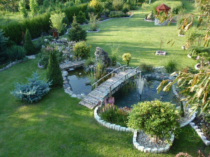 an aerial view of a garden with a pond and bridge in the center, surrounded by lush green grass