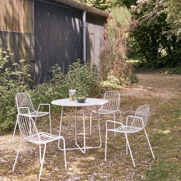 three white chairs and a table outside in the grass