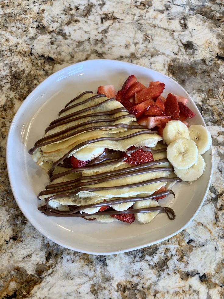 a white plate topped with sliced bananas and strawberries next to chocolate drizzle