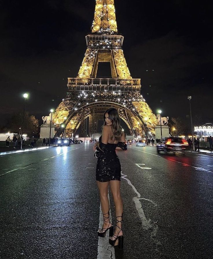 a woman standing in front of the eiffel tower at night with her hand on her hip