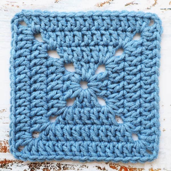 a blue crocheted square with holes in the middle