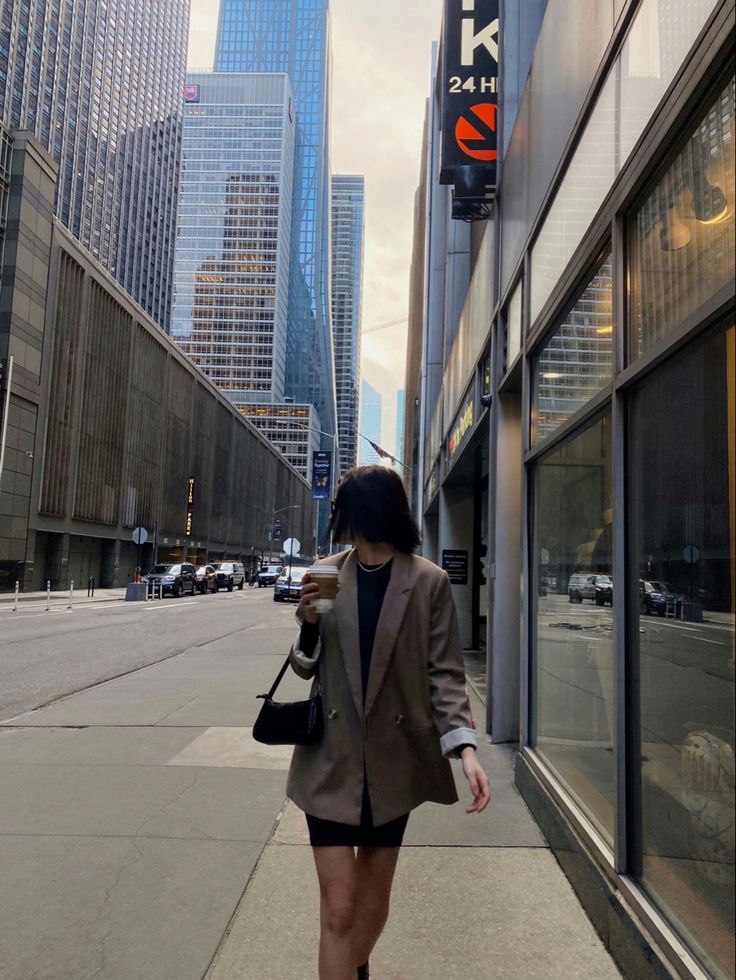 a woman is walking down the sidewalk with her cell phone in her hand and she is wearing a blazer