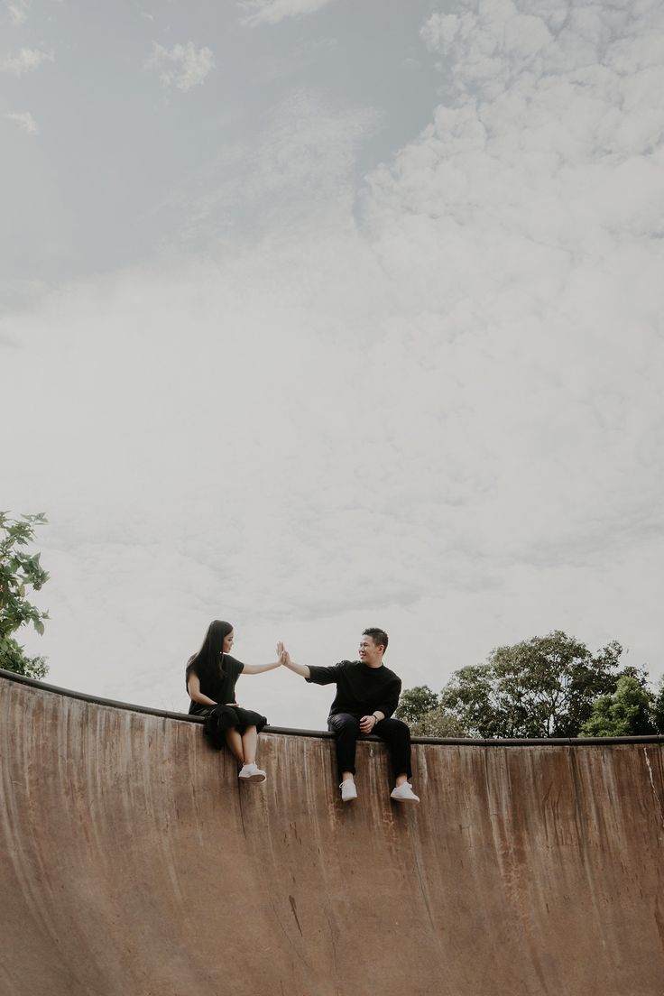 two people sitting on the edge of a skateboard ramp, one holding his hand