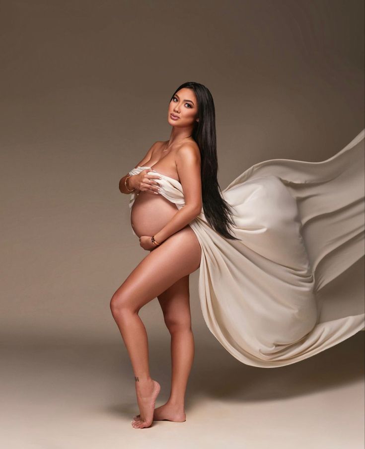 a pregnant woman in a white dress posing for the camera with her long black hair