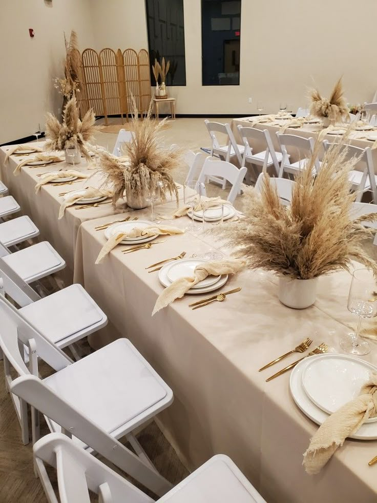 the table is set for an event with white chairs and tables covered in beige linens