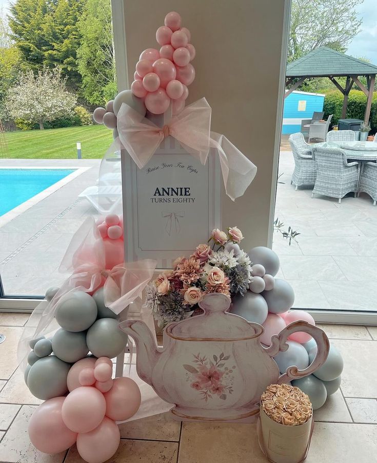 a tea pot with balloons and flowers in front of a pool