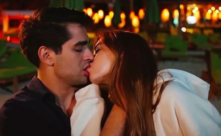 a man and woman kissing each other in front of an outdoor area with lights behind them