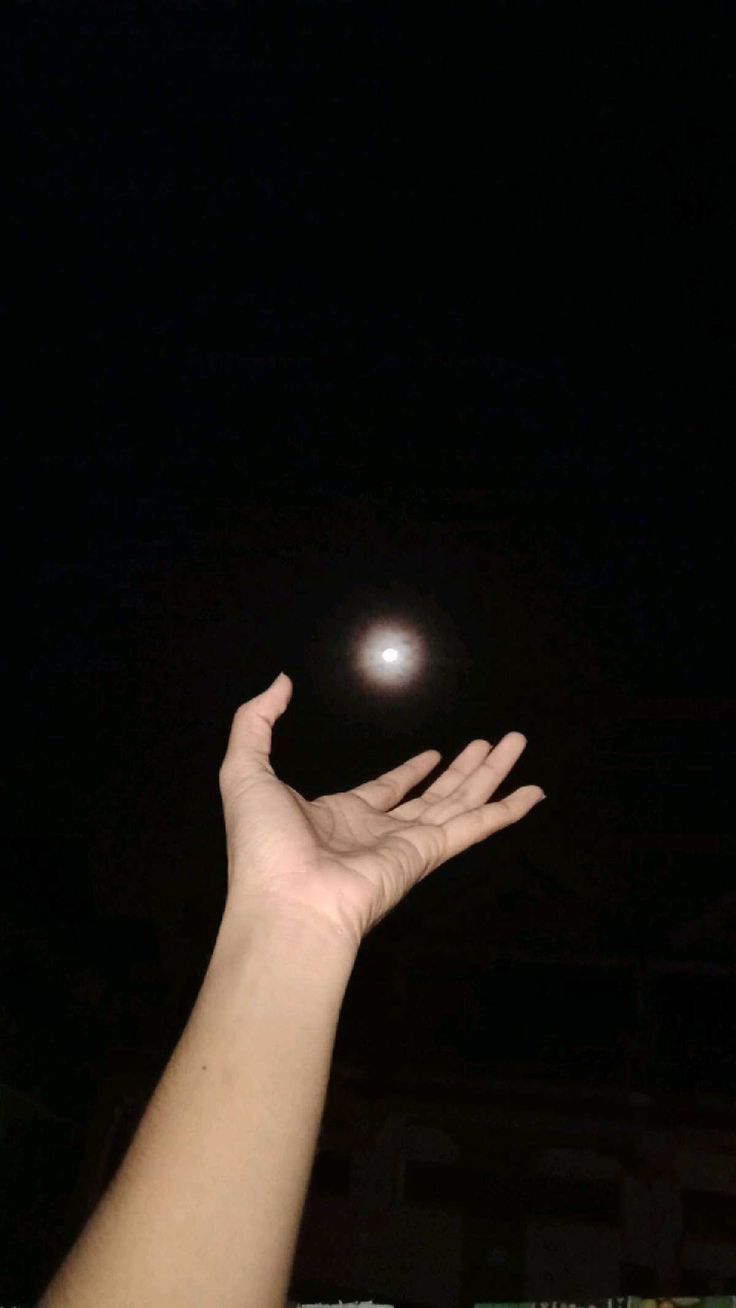 a person reaching up to catch a frisbee in the dark sky at night