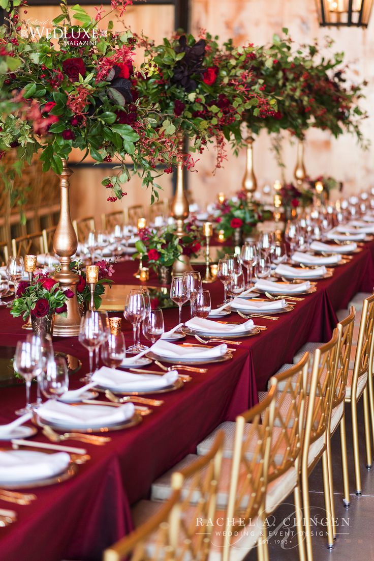 a long table is set up with red and gold place settings for an elegant dinner