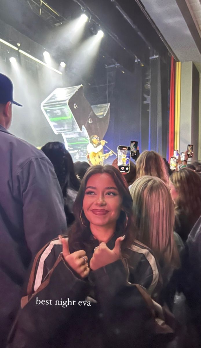 a woman giving the thumbs up sign in front of a group of people at a concert