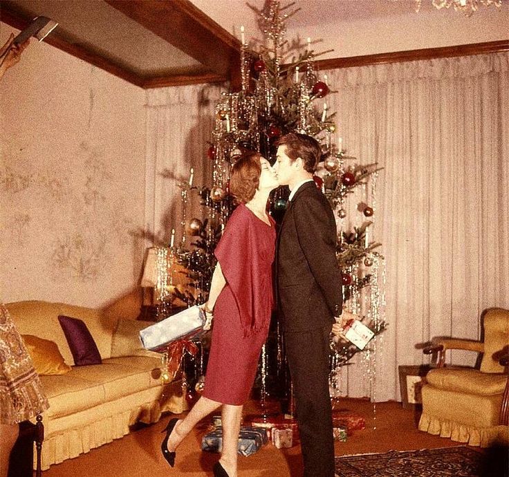 a man and woman kissing in front of a christmas tree with presents on it's feet