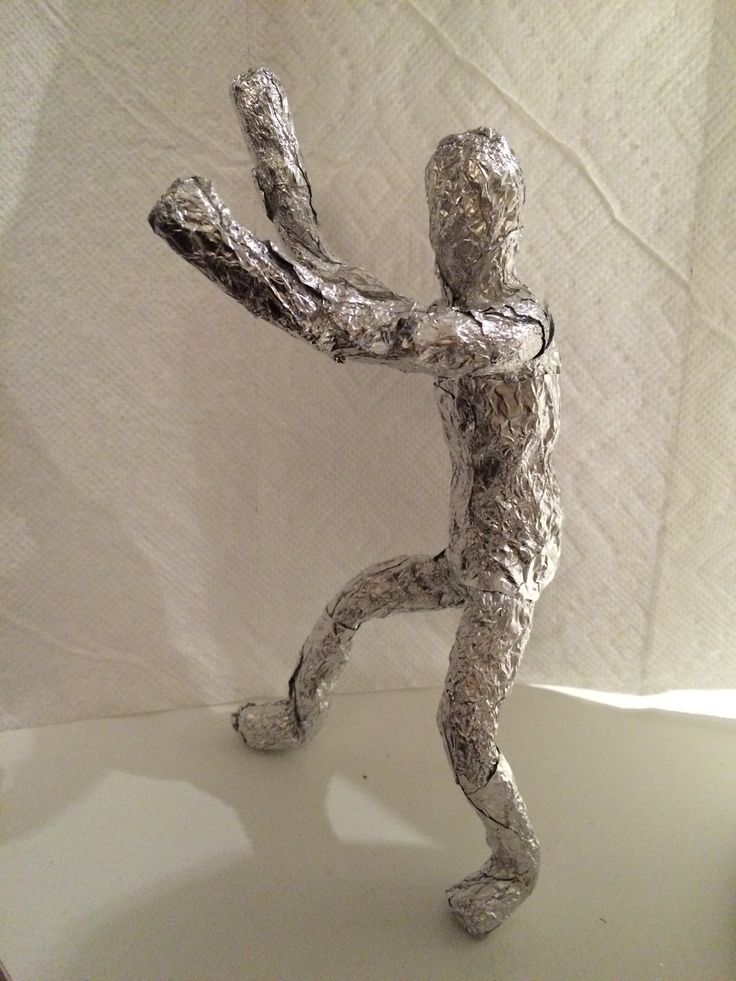 a silver figurine is posed on a white surface