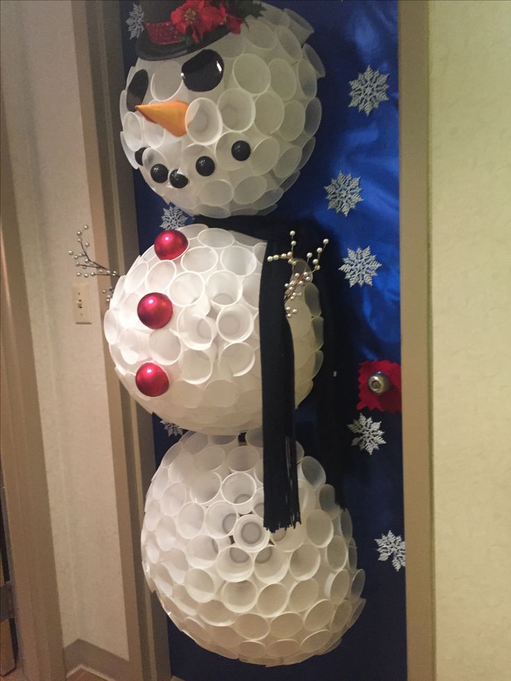 two snowmen made out of plastic cups on the front door, one is wearing a hat