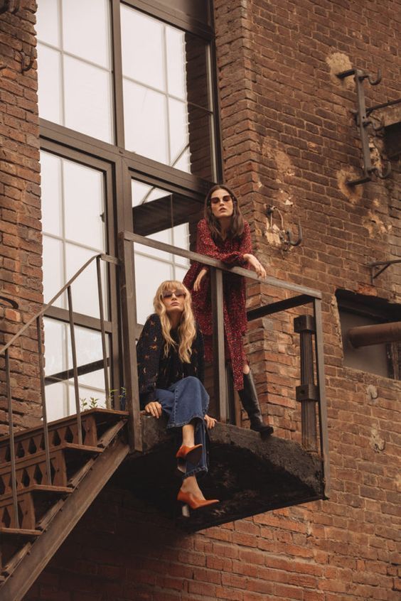 two women are sitting on the stairs outside an old building and one is leaning up against the railing