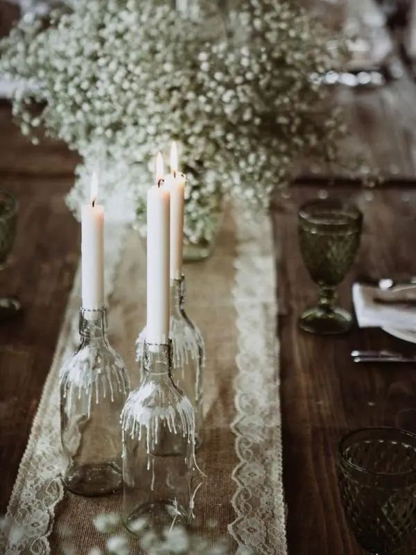 the table is set with candles and glass vases on top of lace runnering