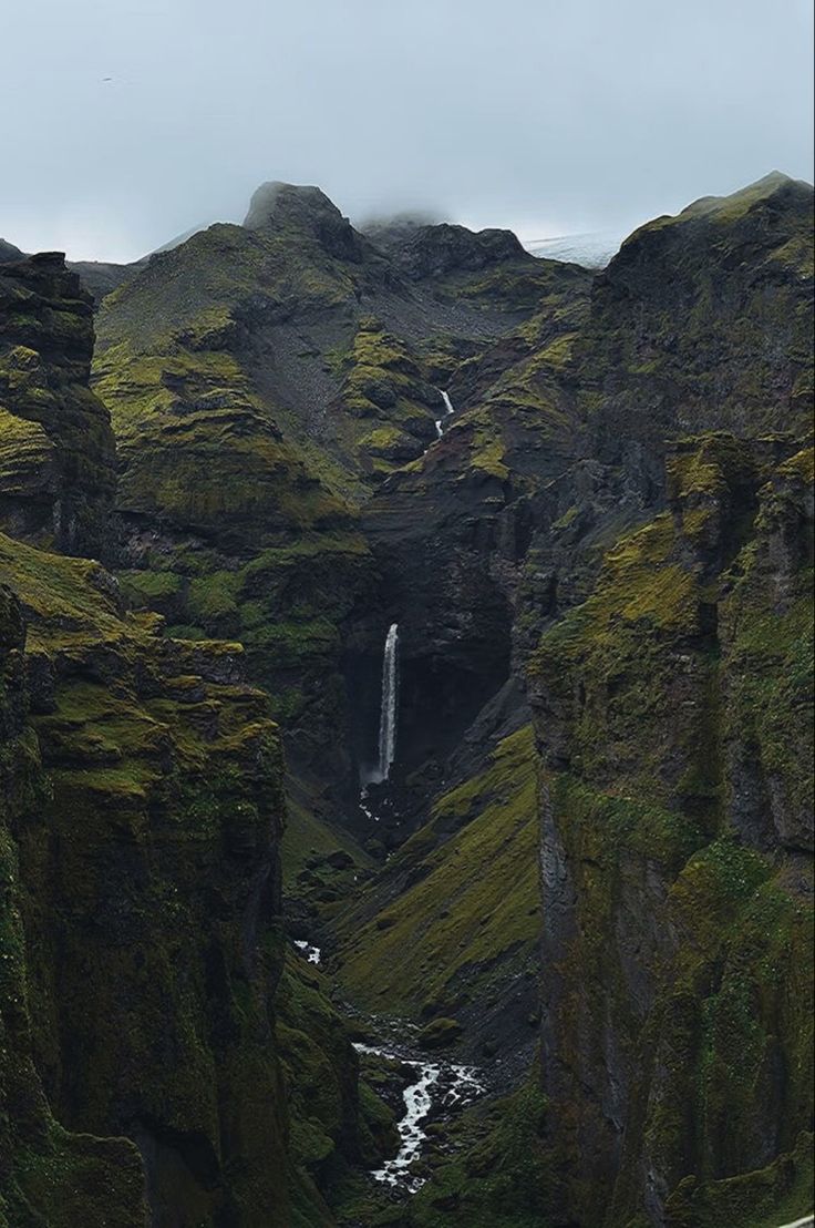 there is a waterfall in the middle of this mountain side area with moss growing on it