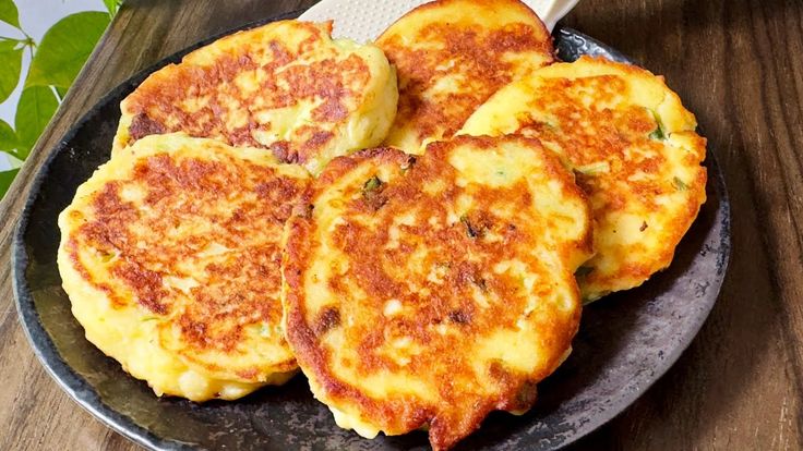 three pancakes on a black plate with a spatula next to it and green leaves in the background