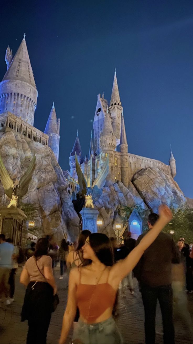 a woman standing in front of hogwarts castle at night with her arms up