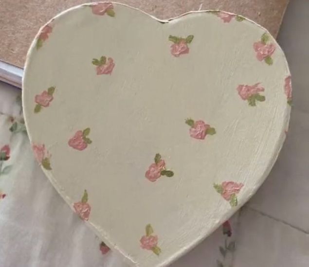 a heart shaped box sitting on top of a bed covered in pink flowers and leaves